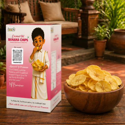 A box of Pranavan Foods Coconut Oil Banana Chips is shown next to a wooden bowl filled with the golden-brown banana chips on a wooden table, with a traditional Indian patio background.
