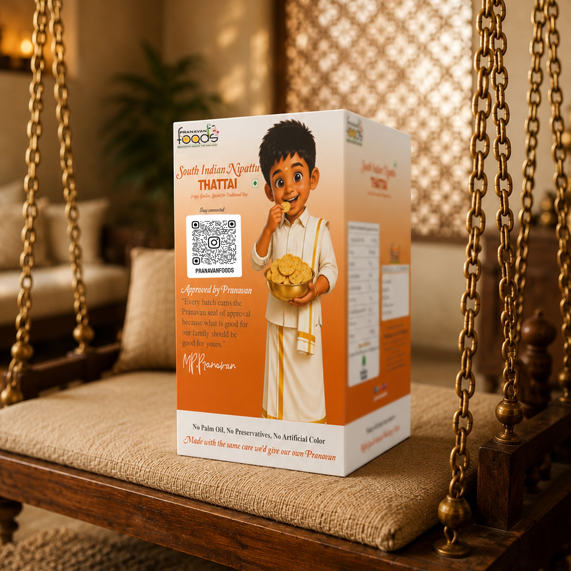 A boxed Pranavan food product labeled 'South Indian Thattai' stands on a wooden swing chair in a warm indoor setting. The package is predominantly white and orange with printed illustrations and text, including a QR code and a child in traditional clothing.