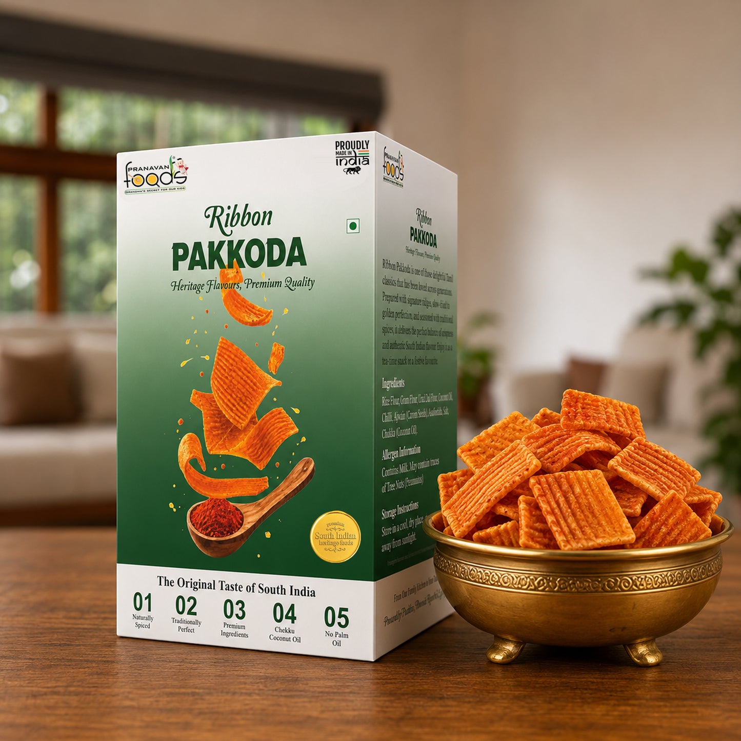 A box of Pranavan Foods Ribbon Pakkoda snack crackers sits on a wooden table next to a gold-colored bowl filled with the orange-brown square crackers, set against a blurred indoor background.