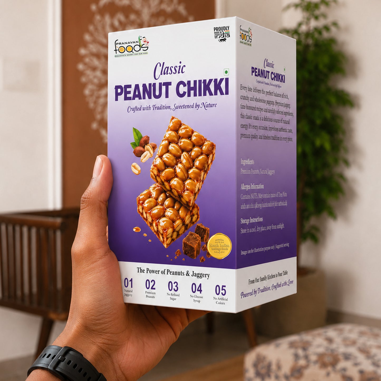 A hand holds a box of Peanut Chikki against an indoor background with a wooden chair and plant. The box is white and purple with images of peanut chikki bars and text detailing the product.
