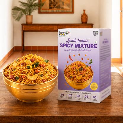 A bowl of South Indian Spicy Mixture snack mix is shown next to its retail packaging box on a wooden table, with a warm, blurred indoor background.