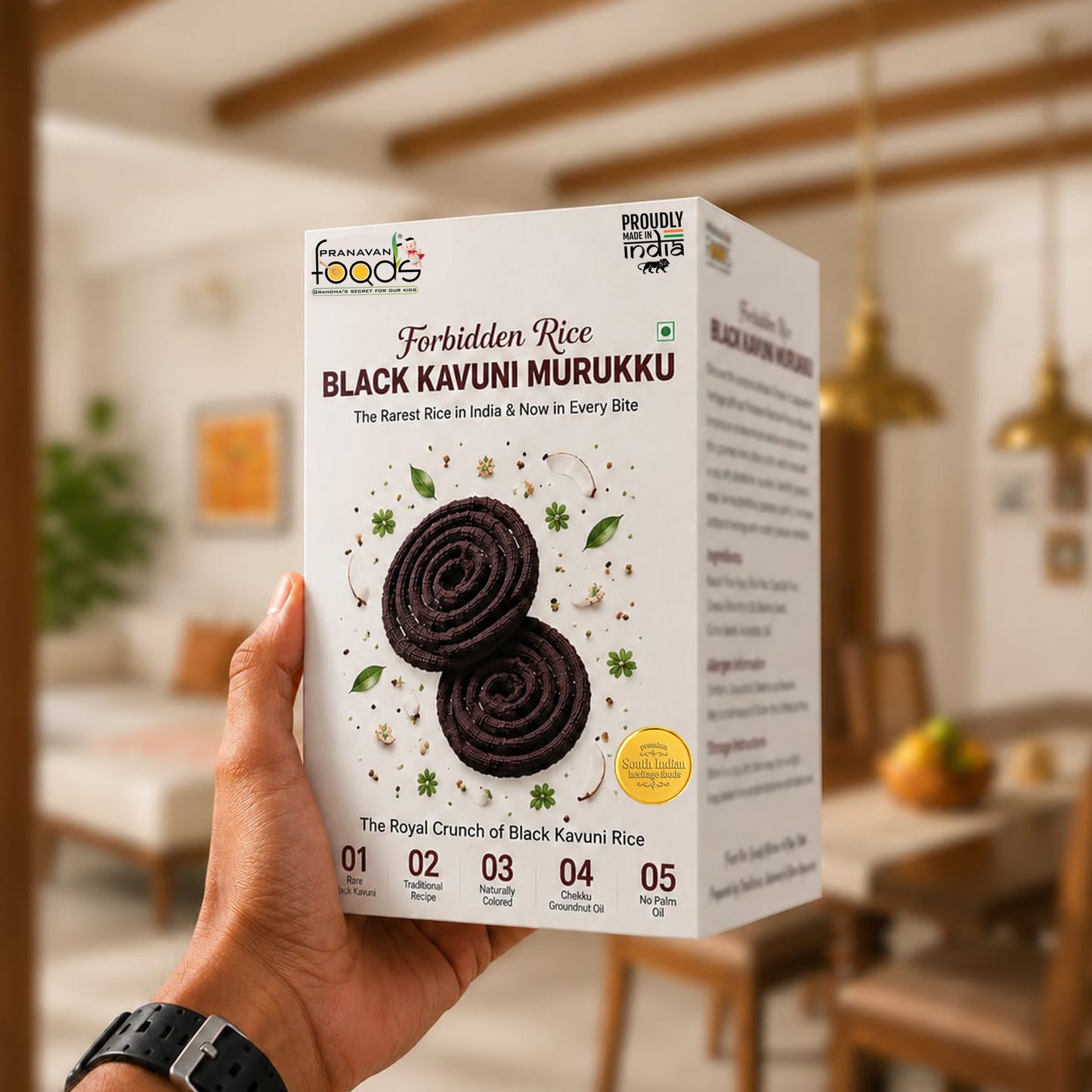 A hand holds a white box of Pranavan Foods Forbidden Rice Black Kavuni Murukku against a blurred indoor home background.
