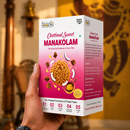 A hand holding a box of Chettinad Sweet Manakolam (deep-fried coconut slices) against a blurred golden background of an ornate interior.