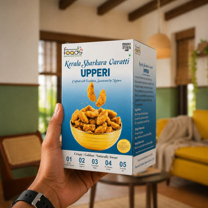 A hand holds a box of Kerala Sharkara varatti Upperi crispy fried snacks in a cozy, softly blurred indoor setting with warm lighting and wooden furniture.