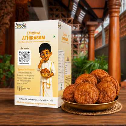 A box of Pranavan Foods Chettinad Athirasam ladoo cookies stands on a wooden table next to a gold plate filled with the round, golden-brown cookies. The background shows a blurred traditional wooden structure.